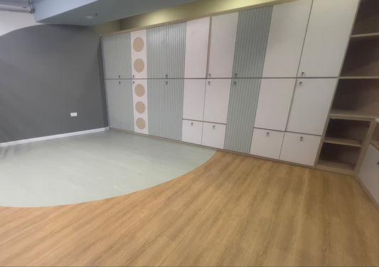 工程案例的東華三院屯門綜合服務中心的房間採用淺色木材和綠色的雙色地板。牆上擺放著帶有素色和圖案門的儲物櫃,右側設有開放式層架。.