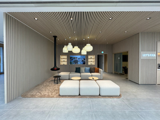 現代休息室展示了工程案例的沃爾沃車行展廳,配有灰色組合沙發、木質天花板、吊燈、壁掛式電視和“Let's Fika”標誌。.