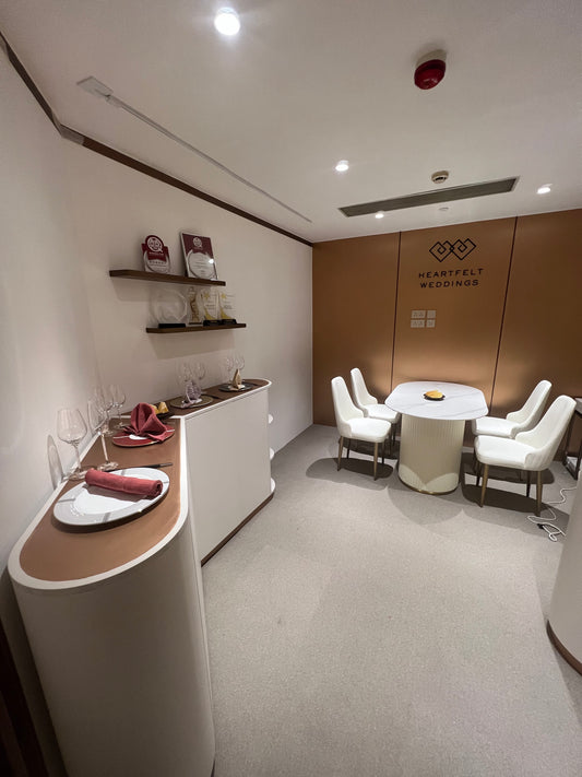 旺角朗豪坊Cordis 酒店的典雅客房配有一張圓桌和六把白色椅子,由工程案例提供。裝飾包括擺放著獎品、餐巾和玻璃器皿的架子。牆上裝飾著“Heartfelt Weddings”的標誌。室內以中性色調為主。.