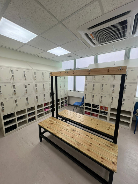 惠康總公司更衣室,工程案例:白色儲物櫃,中央有木製長凳和掛鉤、藍色椅子和天花板上的空調設備。.