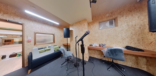 工程案例落成的香港遊樂場合作賽馬會上葵湧青少年綜合服務中心,設有木牆、麥克風架、沙發和兩張椅子的音樂工作室;俯瞰另一個房間的窗戶;桌上型揚聲器;和天花板燈。.